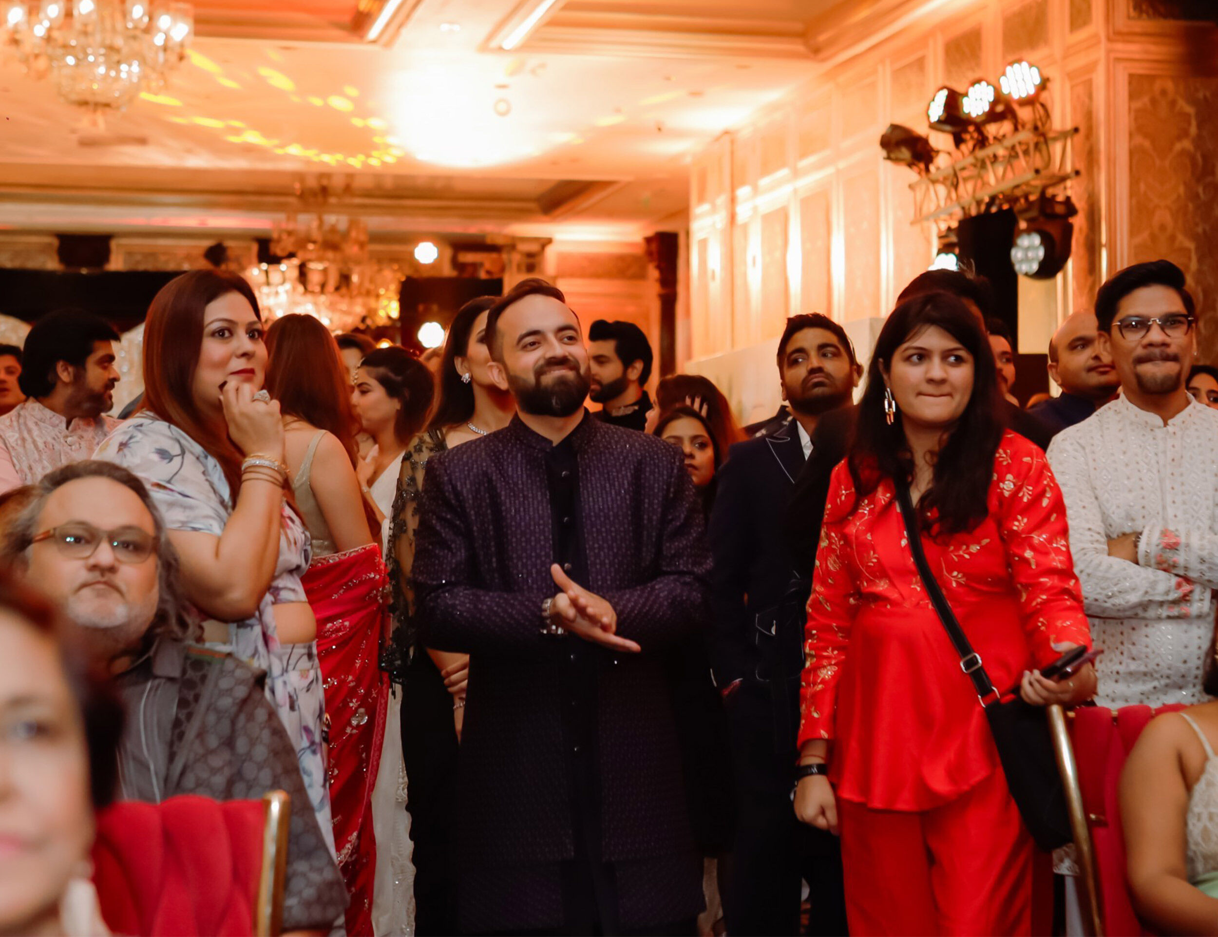 Guests dressed in festive Indian ethnic wear and fusion outfits enjoying an indoor wedding event with warm lighting and elegant décor.